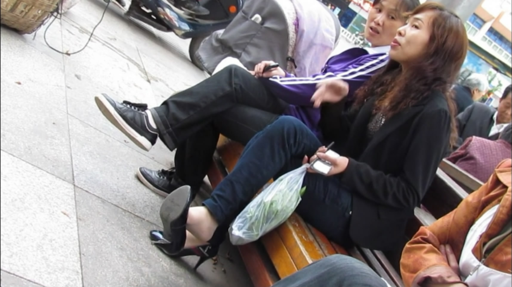 Two women dangle their black high heels on their pale nylon feet.